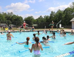 Children in a pool with pool noodles in hand.